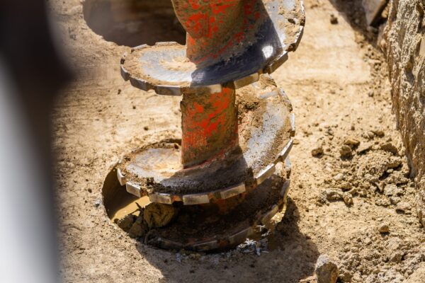Close-up of an auger drill cutting into the ground during drilling services and foundation construction. The image highlights construction drill work, anchoring and piling, bored piles, site preparation and civil construction by specialist civil contractors.
