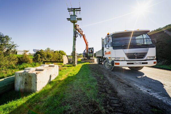 Excavator-mounted auger operating beside a truck during drilling services and civil construction works along a roadside site. The image shows civil contractors managing construction drill operations, site preparation, machinery transport, utility infrastructure and project management.