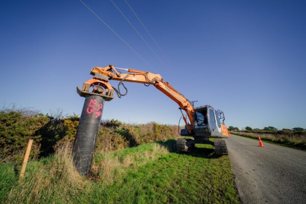 Excavator completing piling contractors work beside a road, installing a large driven pile for civil construction and foundation construction. The image highlights civil contractors delivering anchoring and piling, utility infrastructure, site preparation and project management on a roadside construction site.