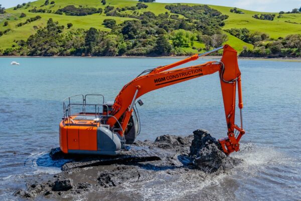 Excavator carrying out marine excavation and excavation and dredging works in shallow water as part of marine construction and coastal construction. The image shows marine contractors and civil contractors completing siteworks, marine services and project management for a waterway construction project.