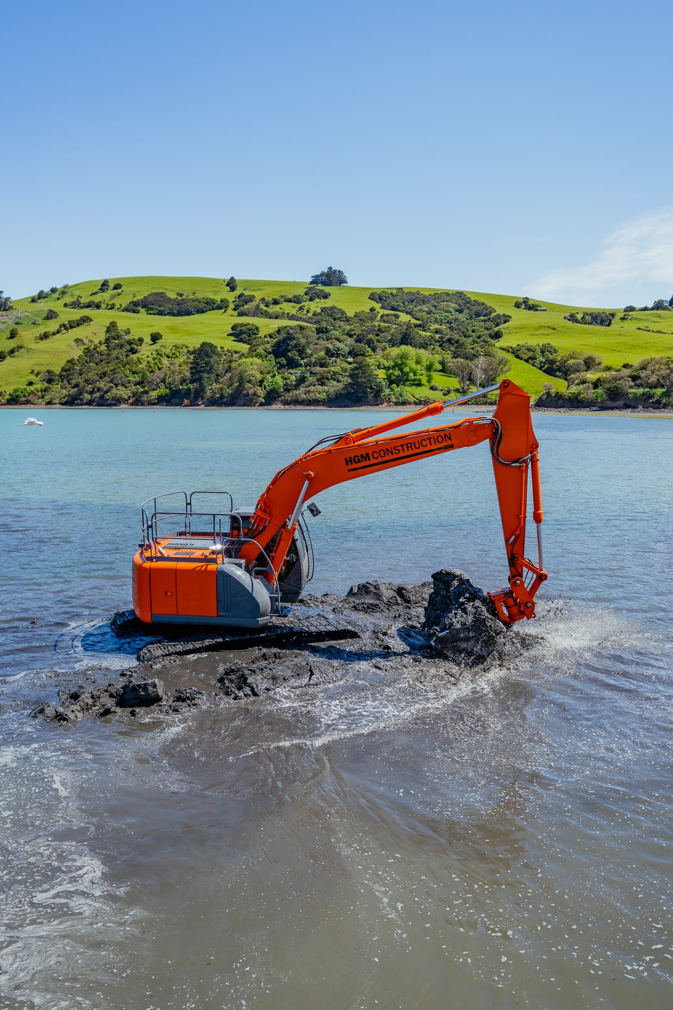 Excavator carrying out marine excavation and excavation and dredging works in shallow water as part of marine construction and coastal construction. The image shows marine contractors and civil contractors completing siteworks, marine services and project management for a waterway construction project.