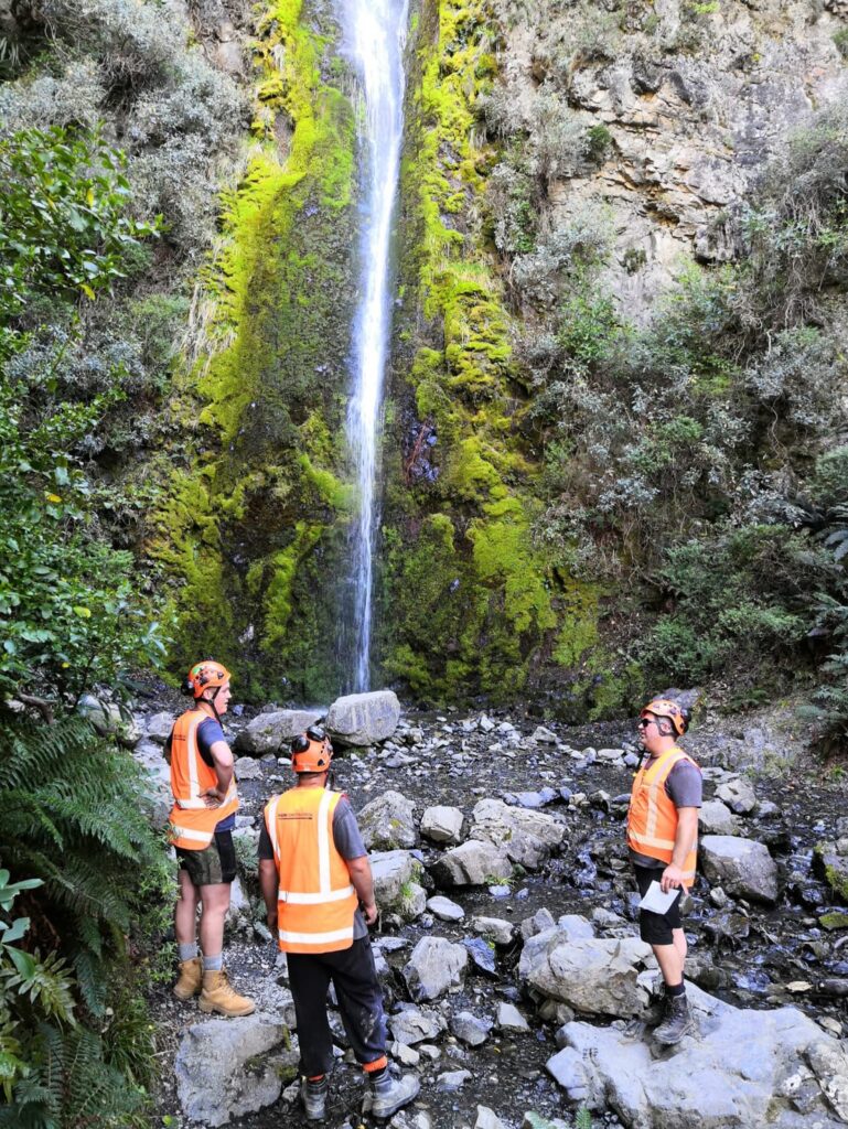 Civil contractors standing near a waterfall during walking track construction and recreation construction works in a rocky natural reserve. The image highlights park construction, site preparation, erosion control and project management for improved public access through the Hanmer waterfall track.
