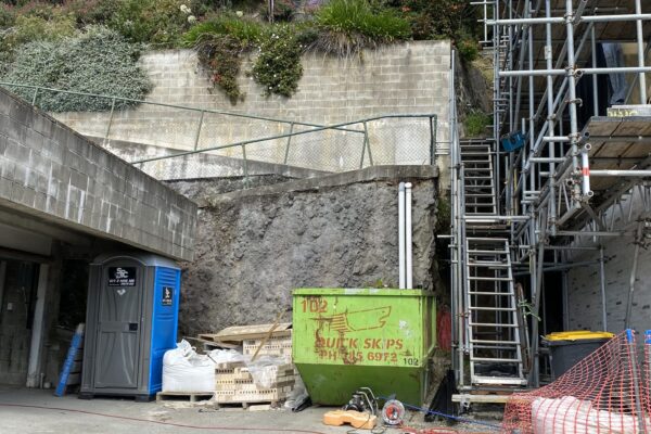 Retaining walls and civil construction works at a steep residential site, with scaffolding, temporary fencing and site preparation underway beside existing concrete structures. The image shows civil contractors managing excavation, slope retention and complex construction projects in a constrained site environment.