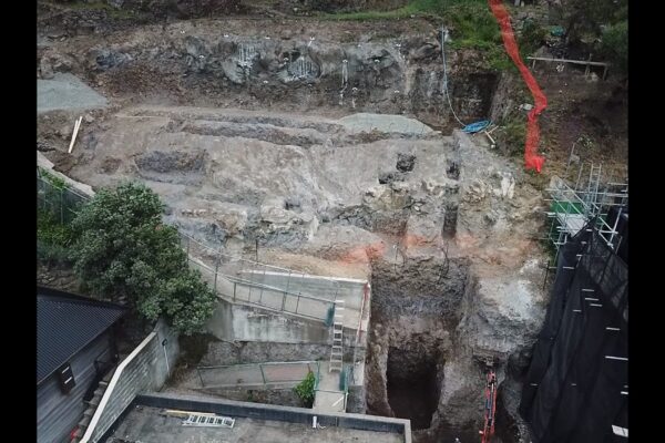 Aerial view of excavation and site preparation for retaining walls, with civil contractors working on a steep rock face between residential buildings. The image highlights civil construction, slope retention, concrete structure preparation, ground stabilisation and foundation construction.