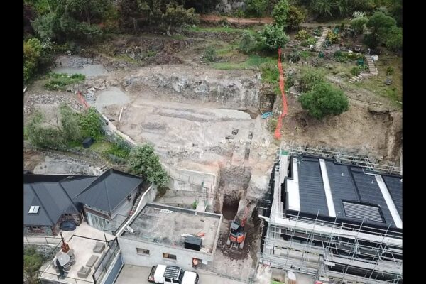 Aerial view of a large excavated hillside site prepared for retaining walls and concrete structure works beside a multi-level residential build. The image shows civil construction, foundation construction, site preparation, bulk earthworks and project management by civil contractors.