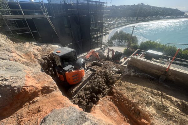 Excavation and retaining walls being constructed on a steep hillside site overlooking the coast, with heavy machinery completing civil construction and siteworks. This image highlights civil contractors, earthworks contractors and site contractors managing slope retention, bulk earthworks and foundation construction in a challenging coastal construction environment.