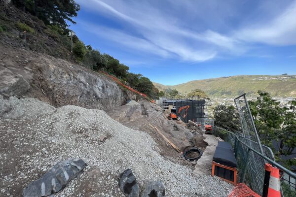 Retaining walls and civil construction underway on a steep coastal site, with excavation, site preparation and rock removal taking place beside temporary safety fencing. The image shows civil contractors managing complex construction projects involving slope retention, ground stabilisation and foundation construction.