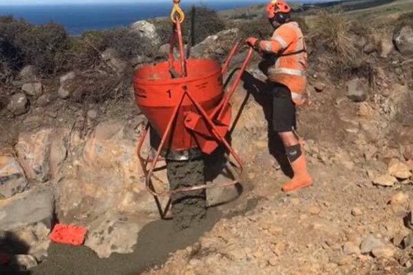 Civil contractor guiding a concrete skip during foundation construction on a remote hilltop tower installation site. This image highlights civil construction, utility infrastructure, concrete structure works, commercial sling operations and site preparation in challenging coastal terrain.