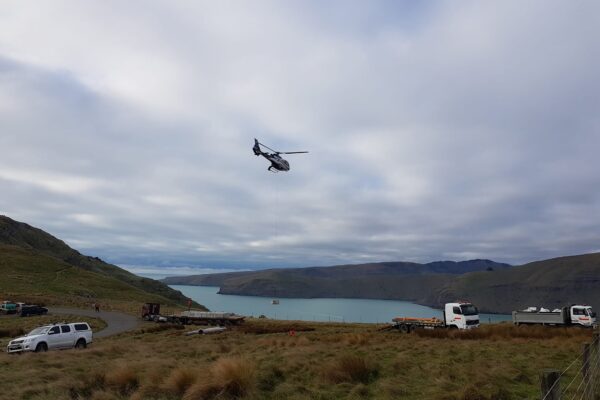 Helicopter operation over a remote hilltop construction site near the harbour, supporting tower installation and civil construction works. The image highlights utility infrastructure, commercial sling operations, site construction and project management by civil contractors in New Zealand.
