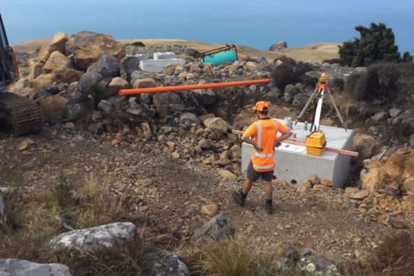 Civil contractors installing concrete foundation blocks on a remote coastal hillside for AIS tower installation and overhead infrastructure. This image highlights utility infrastructure, tower installation, machinery transport, siteworks and project management in difficult access terrain.