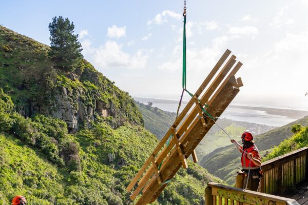 Helicopter operation lifting timber materials into Barnett Park for staircase replacement and walking track construction. The image highlights commercial sling operations, recreation construction, timber structures, park construction and project management in difficult access terrain.