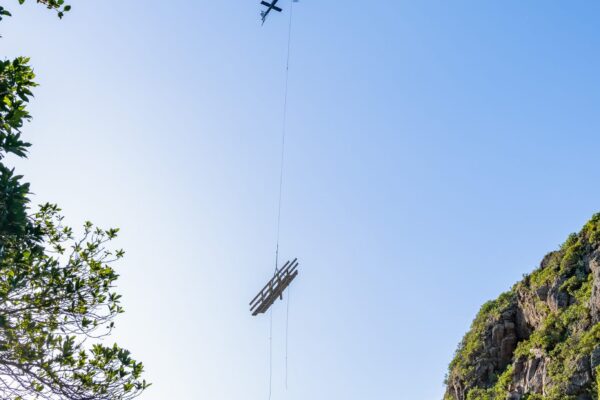 Helicopter operation transporting timber materials through a steep valley for the Barnett Park staircase replacement and walking track construction project. The image highlights commercial sling operations, recreation construction, park construction, site logistics and civil contractors working in difficult terrain.