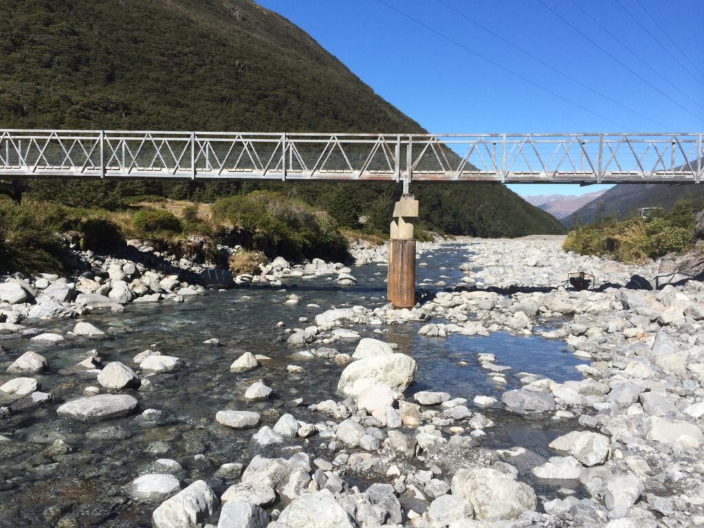 Wide view of a bridge structure spanning a rocky riverbed, with bridge repair and bridge maintenance focused around the central pile support. This image highlights civil construction, bridge inspection services, piling contractors, driven piles and project management in a river environment.