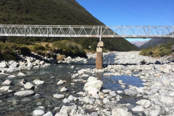 Wide view of a bridge structure spanning a rocky riverbed, with bridge repair and bridge maintenance focused around the central pile support. This image highlights civil construction, bridge inspection services, piling contractors, driven piles and project management in a river environment.