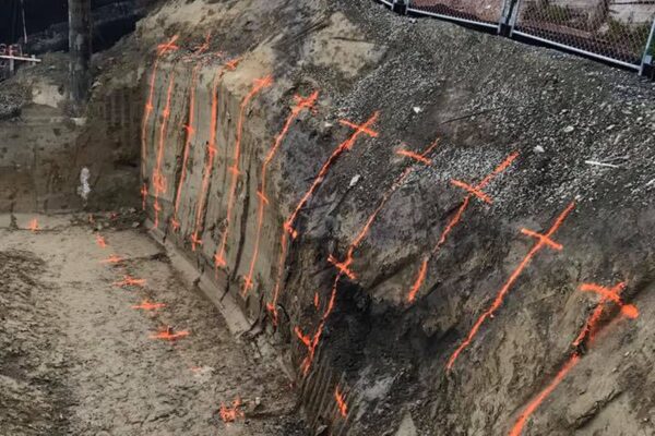 Excavated slope marked out for retaining walls, with soil nails or rock anchors positioned across the bank for slope retention and ground stabilisation. The image shows civil contractors preparing a complex civil construction project involving excavation, siteworks and foundation construction.