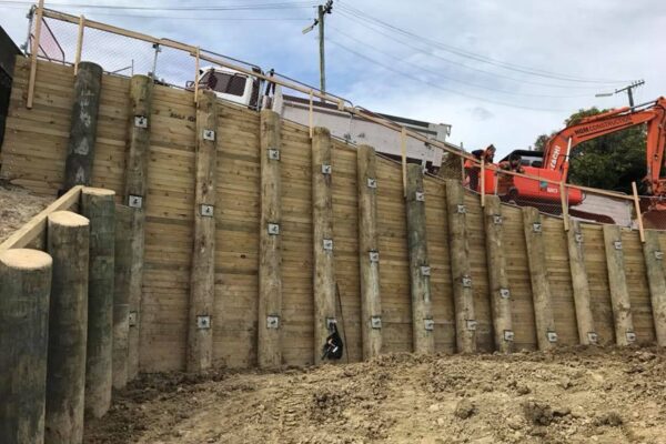 Large scale timber retaining walls completed on a steep site, with mechanical anchors, excavation equipment and civil contractors visible at the top of the structure. This image shows civil construction, slope retention, ground stabilisation, foundation construction and complex project management.