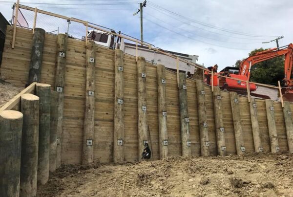Large scale timber retaining walls completed on a steep site, with mechanical anchors, excavation equipment and civil contractors visible at the top of the structure. This image shows civil construction, slope retention, ground stabilisation, foundation construction and complex project management.