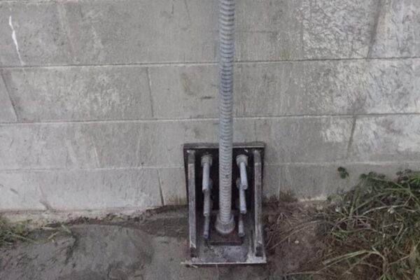 Mechanical anchor system installed through a concrete retaining wall, showing civil construction and ground stabilisation work in detail. This image highlights retaining walls, anchoring and piling, slope retention and concrete structure reinforcement by civil contractors.