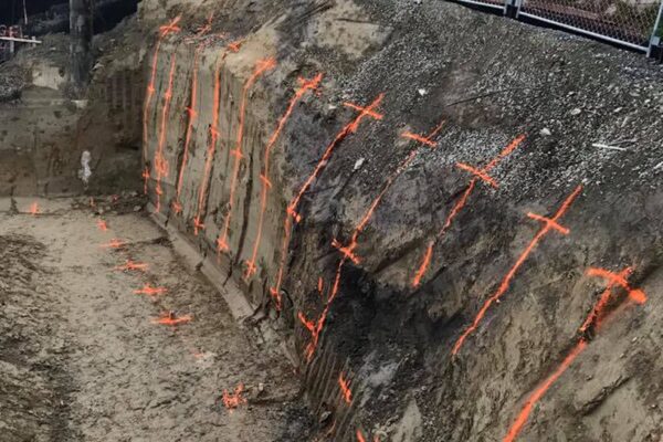 Excavated slope marked for retaining walls and ground stabilisation, with visible rock anchors or soil nails set out across the bank. The image shows civil contractors preparing a complex construction project involving excavation, slope retention and siteworks.