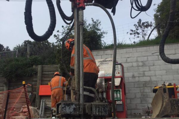 Construction drill and piling equipment working beside a concrete retaining wall during civil construction and foundation construction. This image shows drilling services, anchoring and piling, bored piles, rock anchors and slope retention delivered by civil contractors.