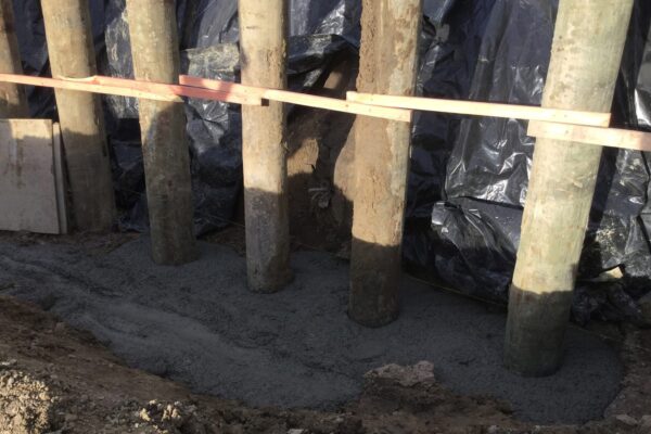 Concrete footing and timber piles forming the base of retaining walls, showing foundation construction and ground stabilisation work in progress. This image shows civil contractors completing concrete structure works, driven piles, slope retention and site preparation for a retaining wall system.
