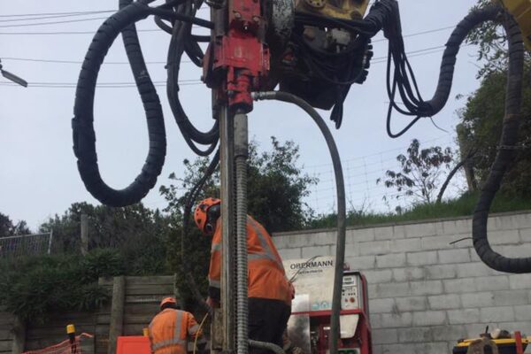 Construction drill and piling equipment operating beside a concrete wall during retaining walls and slope retention works. The image shows drilling services, anchoring and piling, rock anchors, soil nails and civil construction carried out by specialist civil contractors.