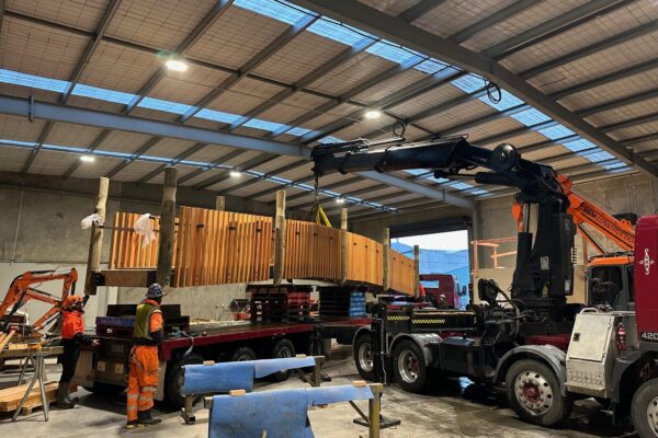 A timber bridge structure being loaded and handled by civil contractors using crane equipment and sling operations during bridge construction. The image shows project management, machinery transport and structure construction for a recreation construction project.