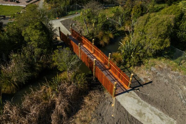 Aerial view of a completed timber bridge crossing a narrow waterway with formed access paths at each end. The project shows bridge construction, civil construction, recreation construction and siteworks within a natural reserve environment.