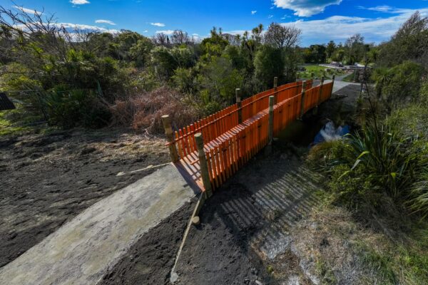 Finished timber bridge crossing a small waterway within a landscaped reserve area. The image shows bridge construction, timber structures, civil construction and recreation construction for public walking access.