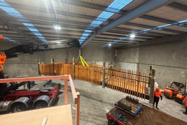 Civil contractors preparing a timber bridge structure inside a workshop before transport and installation. The project highlights bridge construction, timber structures, structure construction, sling operations and careful project management.