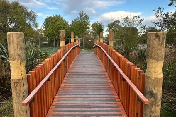 Finished timber bridge construction with timber balustrades and deck boards forming a safe crossing through a reserve. The image shows recreation construction, civil construction, timber structures and siteworks for public access.