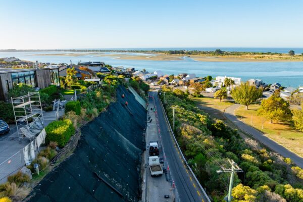 Completed erosion control and slope retention works beside a coastal road, with large areas of rockfall mesh and fencing protecting the hillside. The project demonstrates civil construction, siteworks and ground stabilisation by specialist civil contractors.