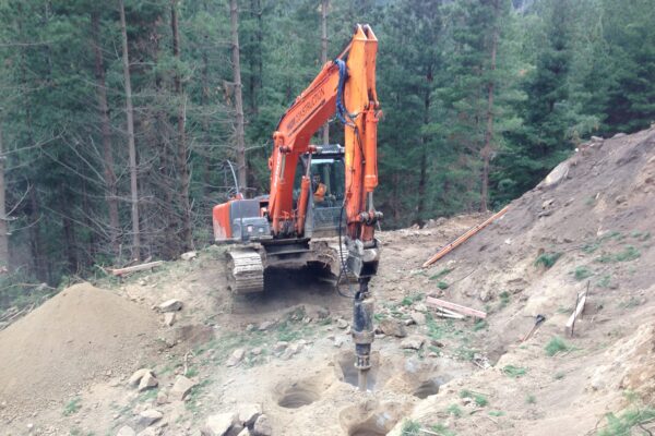 Excavator-mounted drilling equipment completing foundation construction and site preparation on a hillside park construction site. This image shows civil contractors carrying out drilling services, construction drill work, ground stabilisation and adventure infrastructure works.