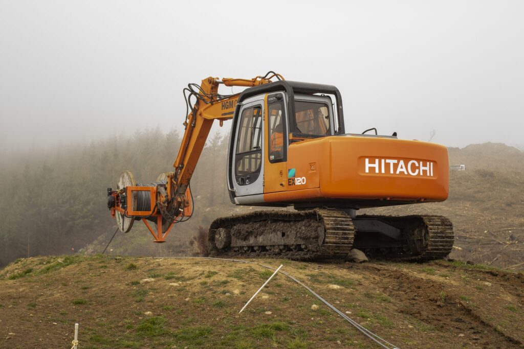 Excavator-mounted construction drill working in misty hillside conditions for adventure infrastructure and civil construction works. The image shows drilling services, rock anchors, soil nails, slope retention and ground stabilisation by civil contractors.