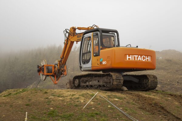 Excavator-mounted construction drill working in misty hillside conditions for adventure infrastructure and civil construction works. The image shows drilling services, rock anchors, soil nails, slope retention and ground stabilisation by civil contractors.