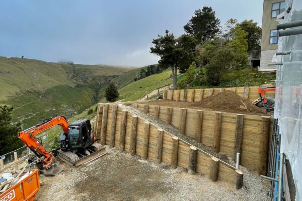 Timber retaining walls under construction on a steep residential site with excavation machinery and gravel backfill in place. The project shows civil construction, slope retention, siteworks and foundation construction by experienced civil contractors.