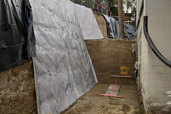 Rockfall mesh and fencing installed along a steep excavation beside a residential building during retaining walls work. The project includes civil construction, slope retention, erosion control and site preparation for a secure concrete structure.