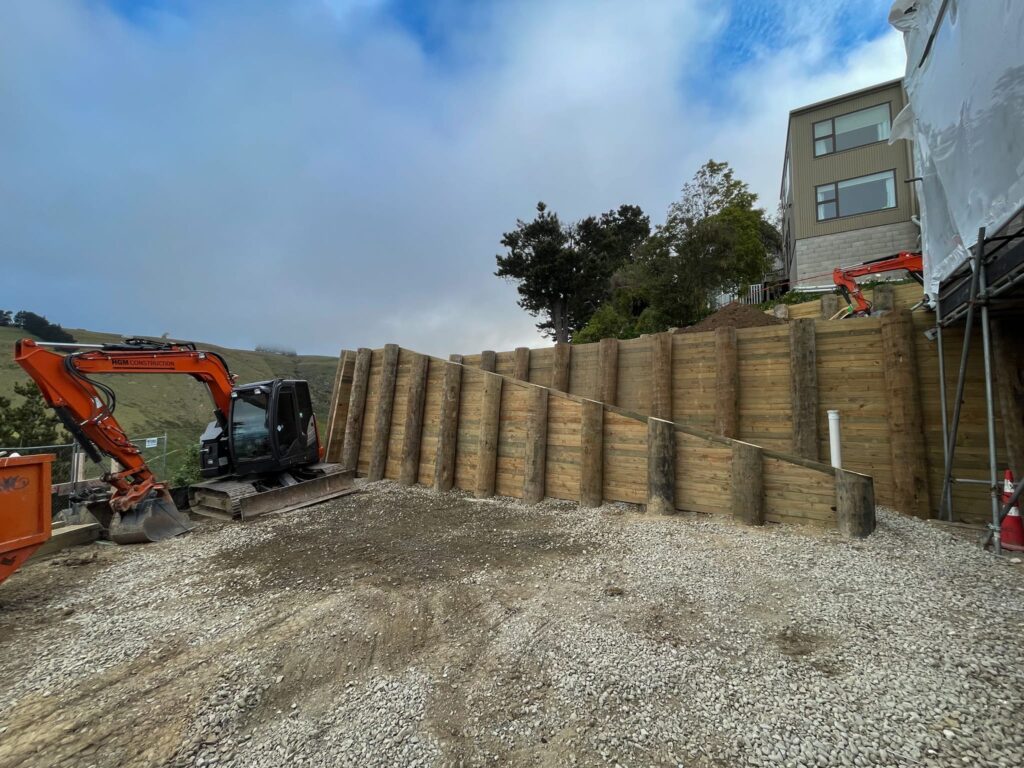 Completed timber retaining walls forming a large scale retaining structure beside a residential building. The image highlights civil construction, slope retention, ground stabilisation and site preparation for a complex hillside construction project.