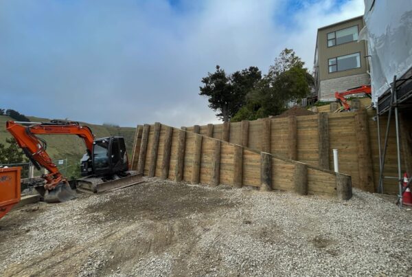 Completed timber retaining walls forming a large scale retaining structure beside a residential building. The image highlights civil construction, slope retention, ground stabilisation and site preparation for a complex hillside construction project.