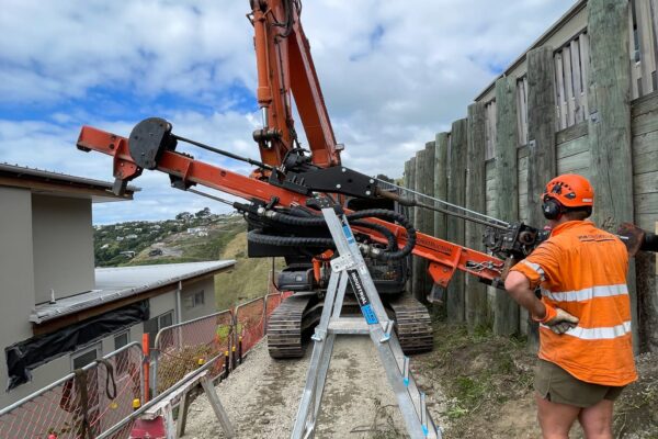 Construction drill set up beside timber retaining walls for piling and slope retention work on a confined residential site. This civil construction project includes drilling services, foundation construction, anchoring and piling, and detailed siteworks.