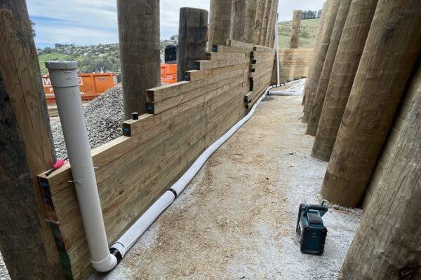 Timber retaining walls under construction with driven piles, drainage pipes and concrete structure preparation on a confined residential site. The work shows civil construction, slope retention, foundation construction and siteworks by specialist civil contractors.