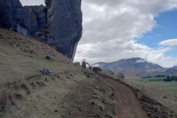Walking track construction underway beside large limestone formations at Kura Tawhiti Castle Hill, with a formed track cut through the hillside. The image shows civil contractors delivering recreation construction, park construction, site preparation, siteworks and erosion control.