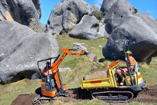 Excavation machinery and civil contractors working between limestone boulders during walking track construction at Kura Tawhiti Castle Hill. The image highlights recreation construction, park construction, site preparation, machinery transport and civil construction in a sensitive reserve setting.