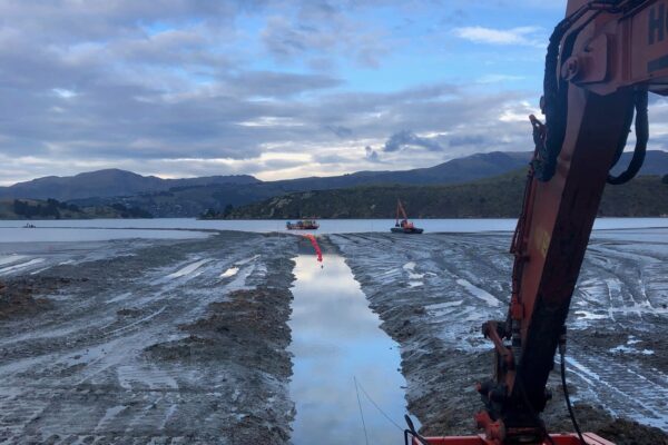 Excavation and dredging works taking place in shallow harbour conditions, with an excavator preparing a trench for utility infrastructure and marine construction. The image highlights marine civil contractors, coastal construction, marine excavation and siteworks for a pipeline project.