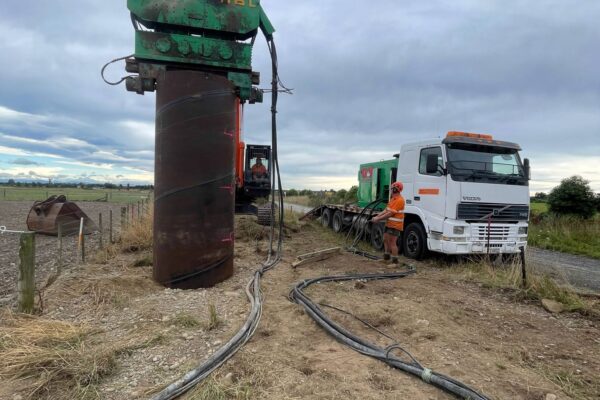 Large steel casing being used for foundation construction on a rural power infrastructure site, with machinery and support vehicles nearby. This image shows civil contractors delivering anchoring and piling, bored piles, utility infrastructure and transmission line construction works.