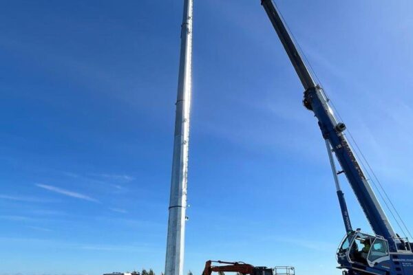 Crane and civil contractors installing a tall pole for power infrastructure and overhead infrastructure works in a rural setting. The image shows tower installation, transmission line construction, site construction and project management for utility infrastructure by civil contractors.