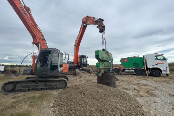 Excavation machinery lifting a large casing during foundation construction for power infrastructure and transmission line construction. The image highlights civil contractors, anchoring and piling, bored piles, site preparation and machinery transport on a rural utility infrastructure site.