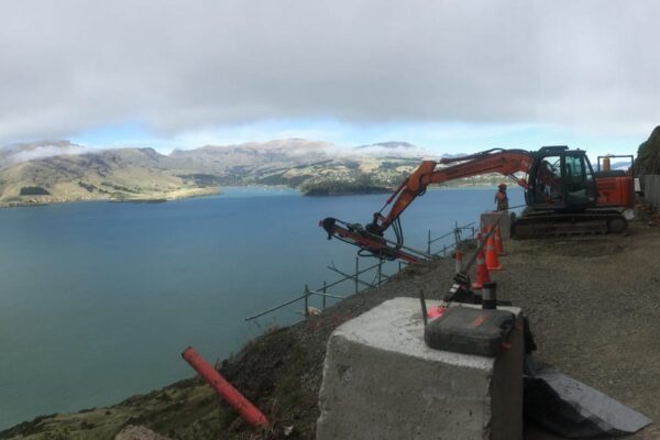 Panoramic view of civil contractors completing anchoring and piling works on a narrow coastal road, with excavation equipment positioned beside safety fencing and harbour views. This image highlights retaining walls, slope retention, rock anchors, site preparation and project management for a challenging civil construction site.