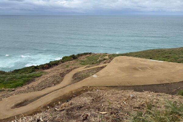 Wide view of walking track construction on a coastal hillside, with a compacted path and formed viewing area overlooking the sea. The image shows civil construction, recreation construction, erosion control and site preparation in a sensitive coastal landscape.