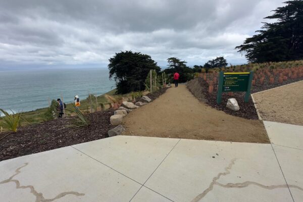 Completed walking track entrance and coastal path with planting, fencing and compacted gravel surfacing leading towards the ocean. The image demonstrates recreation construction, civil construction, siteworks and erosion control for public access.